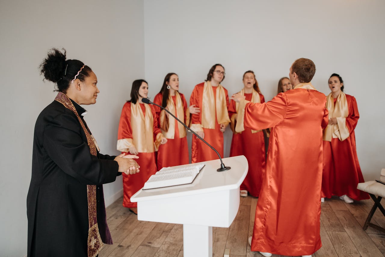 A diverse choir sings passionately during a church service led by a priest in red gowns.